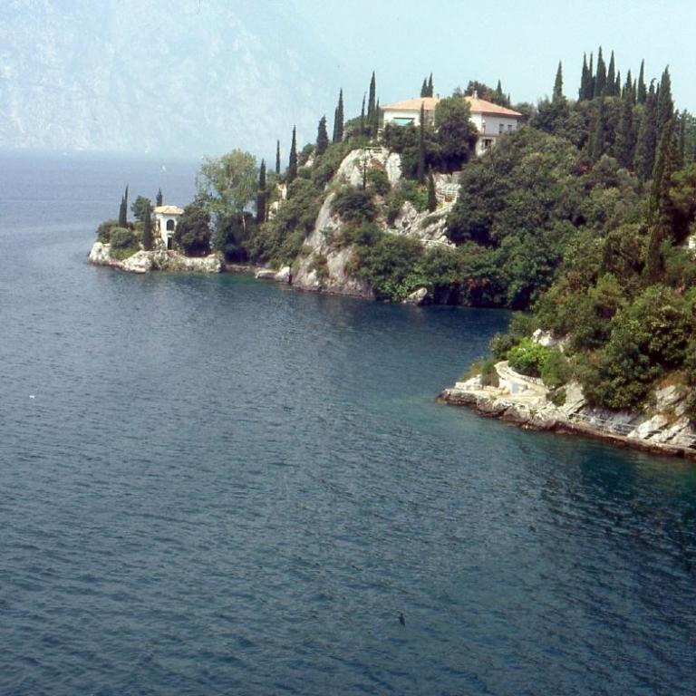 Eine Küstenlandschaft mit einem begrünten Kap, auf dem Häuser und Vegetation stehen, das in das Meer hineinragt.