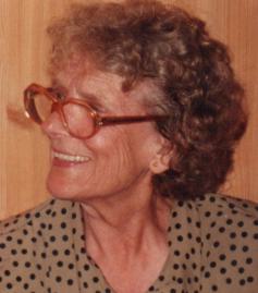 Porträt einer älteren Frau mit voluminösem, lockigem Haar, die eine Brille trägt.