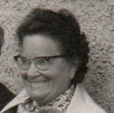 Schwarz-Weiß-Porträt einer älteren Frau mit dunklem Haar und Brille, die lächelt.