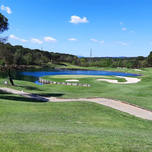 Panoramablick auf einen Golfplatz mit Teich und geschwungenem Pfad unter blauem Himmel.