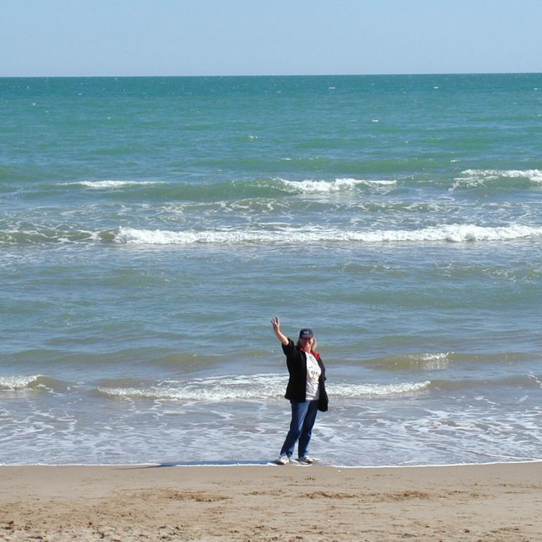Eine Person steht am feuchten Sand und beobachtet die Wellen des Meeres.