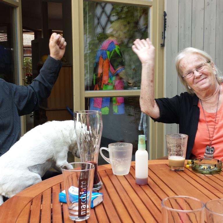 Ein Mann, eine Frau und ein Hund posieren fröhlich auf einer hölzernen Terrasse.
