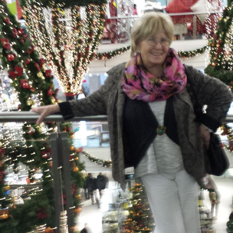 Eine lächelnde Frau steht inmitten von großflächig beleuchteten, festlich geschmückten Weihnachtsbäumen.