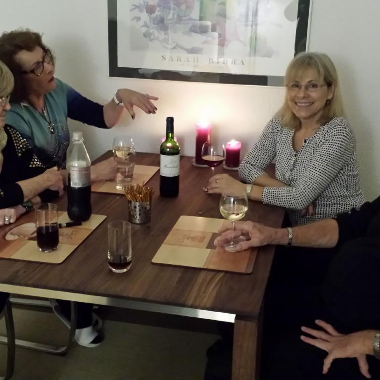 Eine Gruppe von sechs Personen, bestehend aus Frauen und einem Mann, sitzen an einem Holztisch und wirken bei einem Treffen sehr gesellig.
