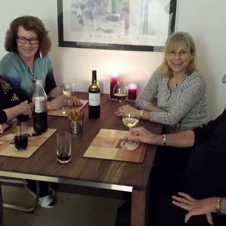Vier Personen, bestehend aus drei Frauen und einem Mann, sitzen an einem Holztisch und führen ein Gespräch.