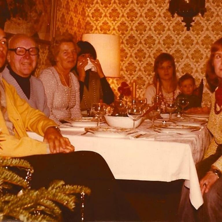 Eine Gruppe von Menschen sitzt an einem gedeckten Tisch und unterhält sich bei einem festlichen Abendessen in einem warm beleuchteten Raum.
