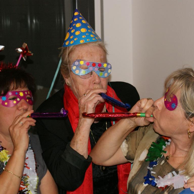 Drei Frauen posieren bei einer Feier, alle tragen bunte Partyhüte und Oversize-Brillen.