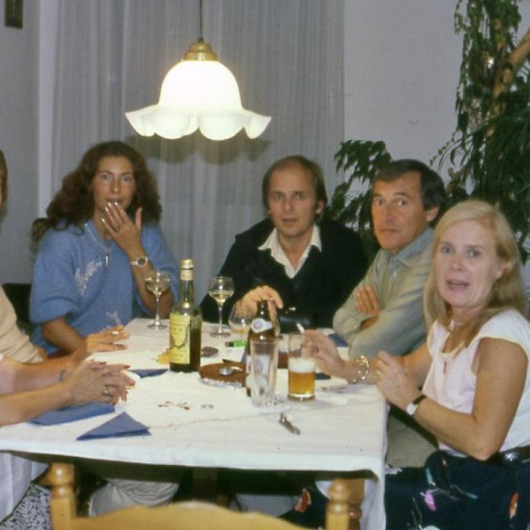 Eine Gruppe von Menschen, bestehend aus Männern und Frauen, sitzt an einem gedeckten Tisch und unterhält sich.