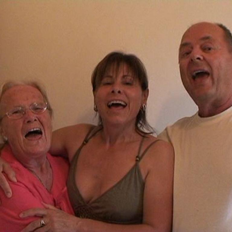 Drei Personen, ein Mann und zwei Frauen, lachen zusammen bei einer Zusammenkunft.