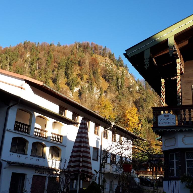 Panoramaansicht eines alpenländlichen Dorfes mit traditionellen Häusern vor einer steilen, bewaldeten Bergkulisse.