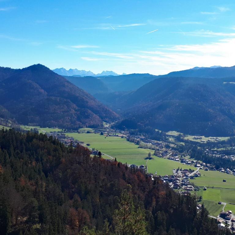 Panoramablick auf ein bewaldetes Bergtal mit kleinen Dörfern in der Ferne.