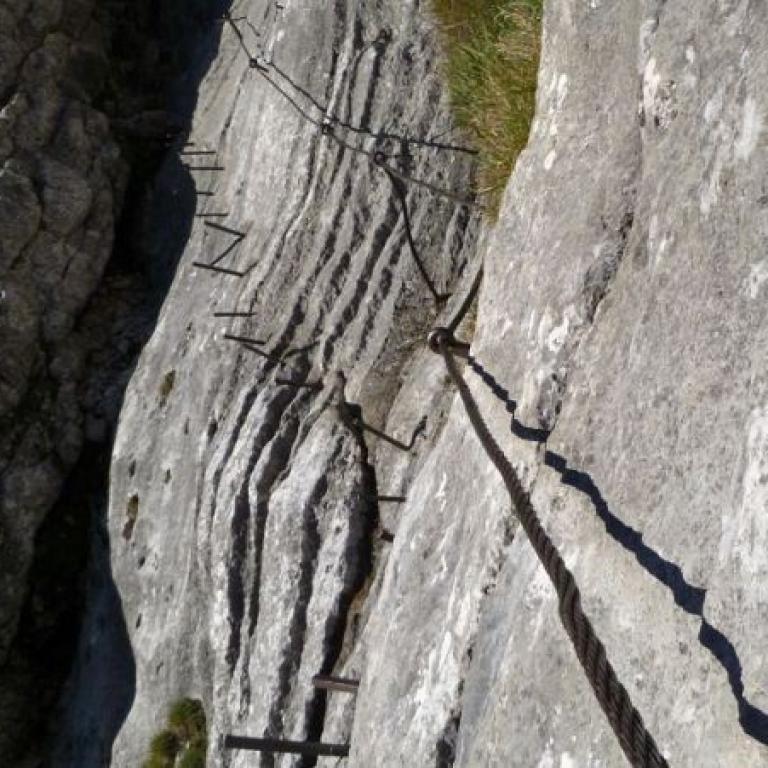 Schmaler Wanderweg entlang einer steilen und felsigen Felswand.