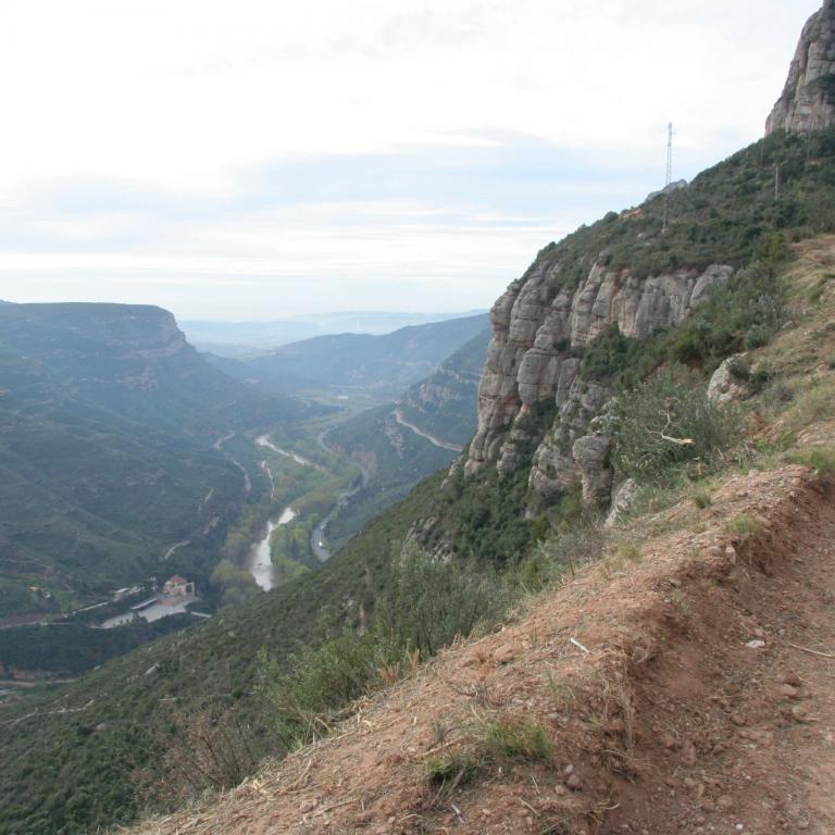 Ein Wanderweg führt entlang eines steilen Berghangs mit Blick auf ein weites Tal und eine Schlucht.