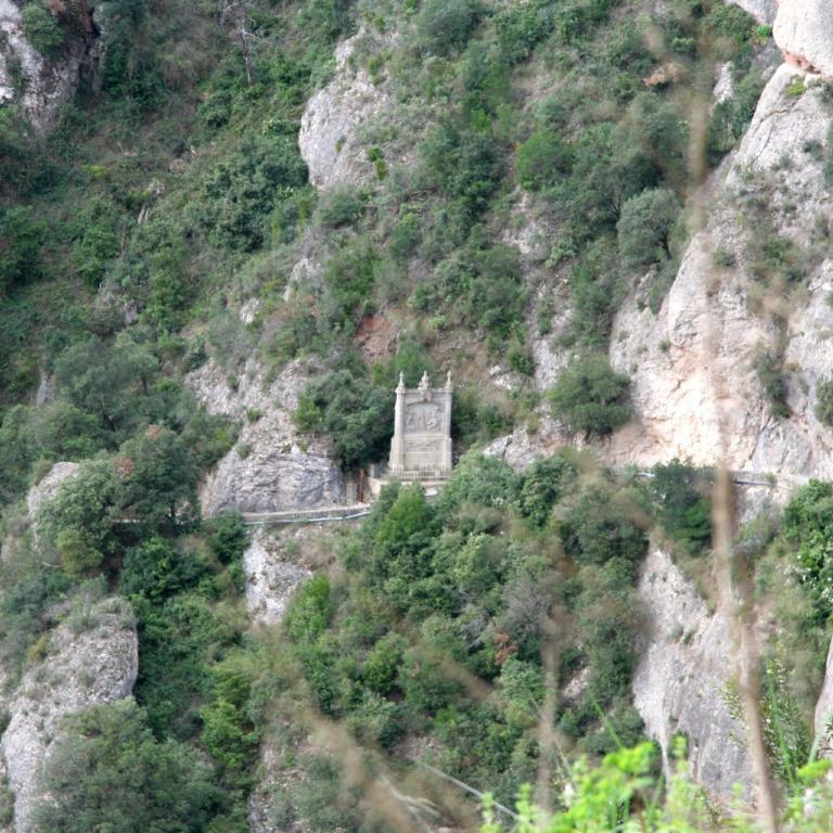 Eine mittelalterliche Burg ist spektakulär in die steil abfallende, bewachsene Felswand eingebettet.