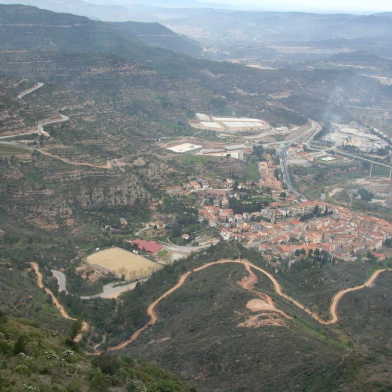 Panoramaaufnahme eines Tals, das von städtischer Bebauung und Straßen durchzogen ist, umgeben von hügeligem Gelände.