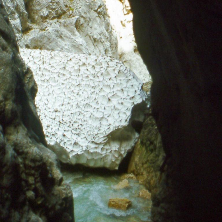 Enger Durchgang in eine Felsgrotte mit hellen mineralischen Ablagerungen.