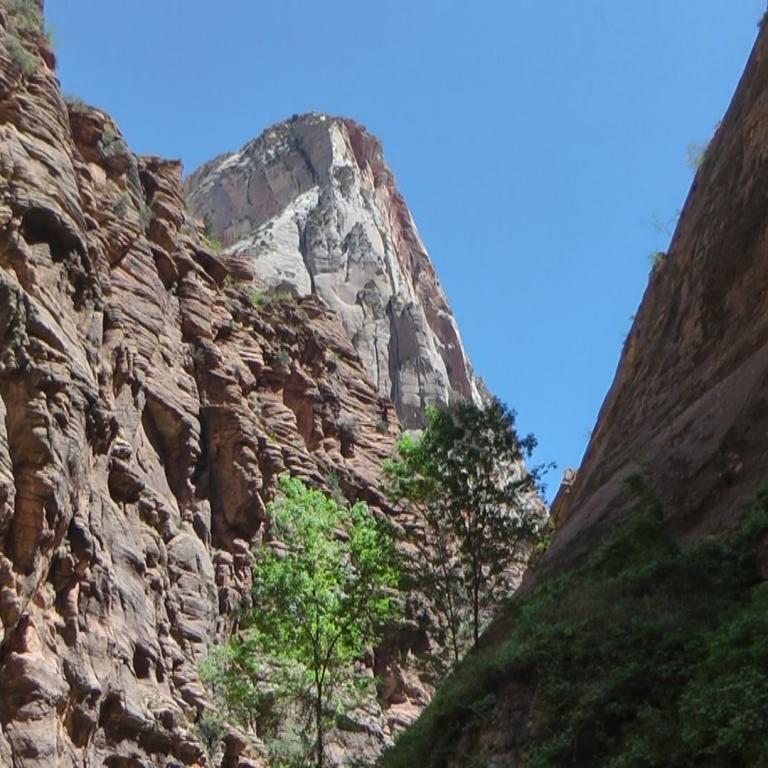 Eine tiefe Schlucht mit steilen, geschichteten Felswänden, die von einem markanten, pyramidenförmigen Gipfel in der Mitte und üppigem Grün im Vordergr