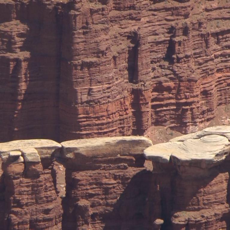 Massive, geschichtete rote Felswände eines Canyonplateaus, im Vordergrund mit gestapelten, erodierten Felsvorsprüngen.