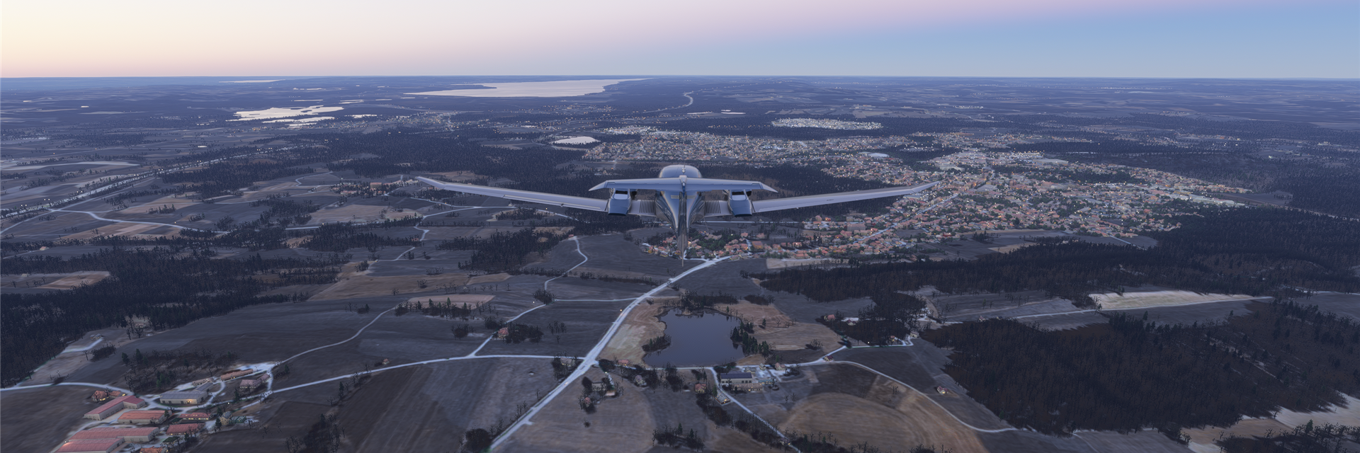 Ein Flugzeug fliegt über eine ausgedehnte, ländliche Landschaft während der Dämmerung.